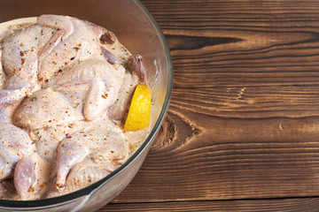Quails marinated in spices with lemon in a glass saucepan on a wooden background. Close-up.