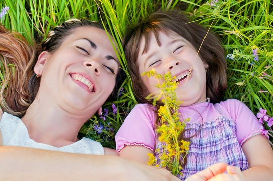 young, beautiful mother with little daughter, happy and laughing on a walk in the grass with flowers on a sunny, summer day. The concept of motherhood and a happy childhood