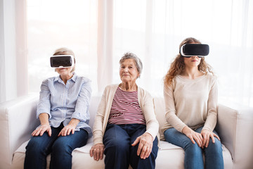 A teenage girl, mother and grandmother with VR goggles at home.