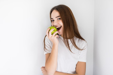 Happy young woman holding an apple and a glass of water sitting on a sofa in the living room at home