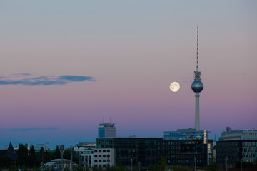 A full moon beside the Berlin TV tower on a peaceful evening sky with urban landscape