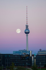 A full moon beside the Berlin TV tower on a peaceful evening sky