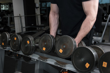 Muscular bodybuilder guy holding big black iron dumbbells in a gym. Man with big hand muscles working out in a gym. Gym and fitness details.