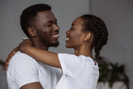 happy young african american couple hugging and smiling each other at home