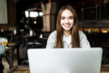Young pretty woman is working on laptop in cafe and smiling.
