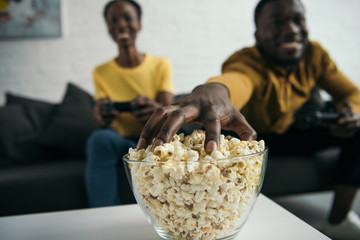 close-up view of young african american couple eating popcorn and playing with joysticks at home