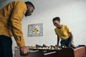 smiling young african american couple playing foosball at home