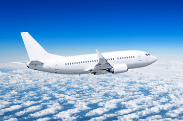Obraz premium Samolot pasażerski leci wysoko nad chmurami i błękitnym niebem.