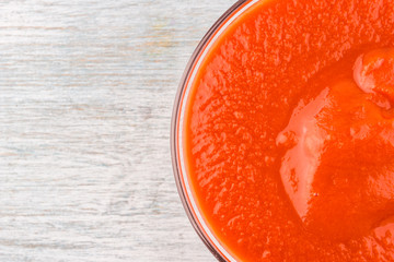 glass cup with tomato paste on a wooden background - close-up, top view