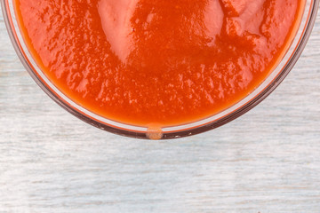 glass cup with tomato paste on a wooden background - close-up, top view