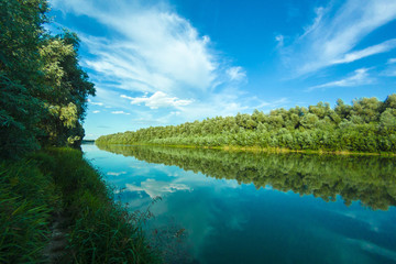 Riverbank of calm Danube river with green trees in spring or summer and deep blue sky with clouds at the setting sun. Ukraine