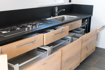 new industrial kitchen detail of open drawers. Kitchen in new apartment in natural oak with granite and steel.