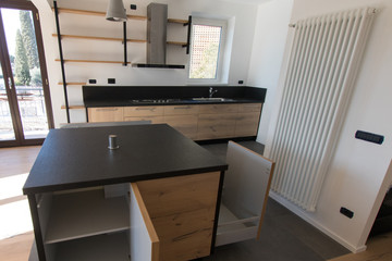 New kitchen in oak and black granite and stainless steel with island, sink, doors, shelves and extractor hood. Industrial design cuisine in a renovated apartment with gray concrete flooring. Cookery