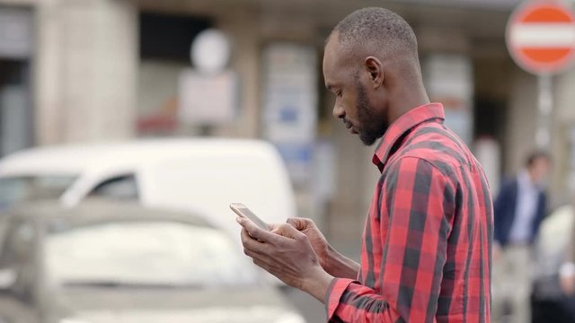 attractive black african man typing on his smartphone in the street