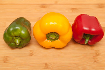 Green, yellow and red pepper on wooden background