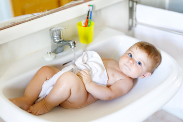 Cute adorable baby taking bath in washing sink and grab water tap.