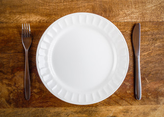 Empty white plate with fork and knife on wooden table, top view