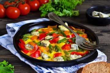 Omelette with vegetables and blue cheese for breakfast on a wooden background.