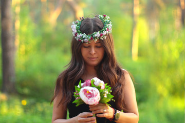 young beautiful woman with a bouquet of flowers and in a wreath in a green park on a sunny summer day