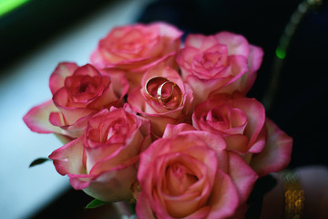 Two gold wedding rings lie on a bouquet of pink roses