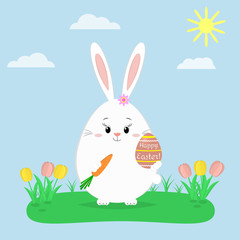 The Easter bunny is standing and is holding a red Easter egg and a carrot. Glade with tulips, sky.