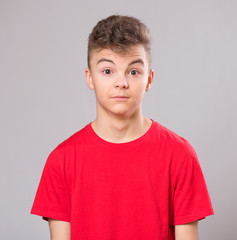 Emotional portrait of caucasian teen boy. Surprised teenager looking at camera. Handsome child wearing red t-shirt, on gray background.