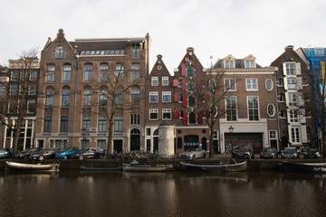 Multicolored houses in Amsterdam on the main canal of the city. Typical Amsterdam Dutch houses with many windows and vertically developed. Boats at bottom