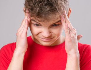 Stress and headache - teen boy having migraine pain. Handsome child suffering from a headache. Unhappy caucasian teenager touching his head, on gray background.