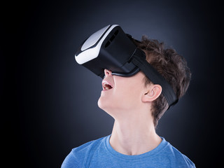 Happy teen boy wearing virtual reality goggles watching movies or playing video games. Cheerful smiling teenager looking in VR glasses. Funny child experiencing 3D gadget technology - close up.