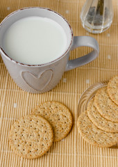 Healthy breakfast: oatmeal cereal, cup of milk, jar of homemade jam, oatmeal cookies. Flowers in a vase on a background. Coconut biscuits on a saucer. Exquisite romantic breakfast. Food blog ideas