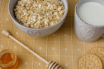 Healthy breakfast: oatmeal cereal, cup of milk, jar of homemade jam, oatmeal cookies. Flowers in a vase on a background. Coconut biscuits on a saucer. Exquisite romantic breakfast. Food blog ideas
