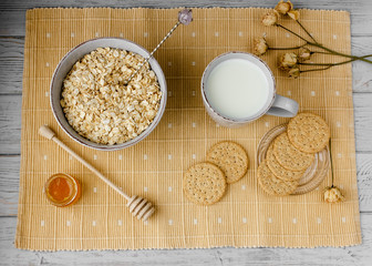 Healthy breakfast: oatmeal cereal, cup of milk, jar of homemade jam, oatmeal cookies. Flowers in a vase on a background. Coconut biscuits on a saucer. Exquisite romantic breakfast. Food blog ideas