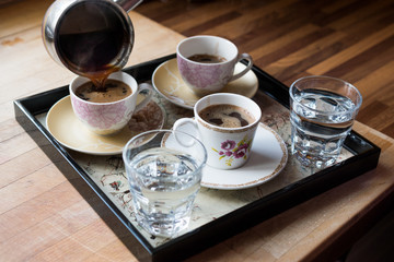 Pouring Turkish Coffee served with water in tray.