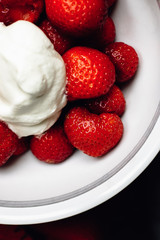 Close up of fresh, ripe strawberries with dollop of whipped cream with sugar in white bowl