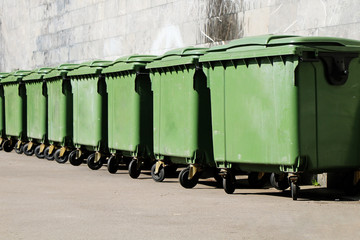A row of green garbage containers on the city street.