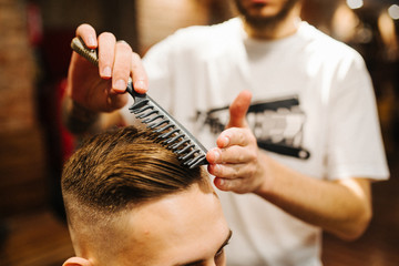 Creating new hair look. Making haircut look perfect. Young bearded man getting haircut by hairdresser while sitting in chair at barbershop