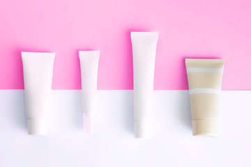 White tubes with beauty cosmetic products; branding mock up; top view on pink colored background