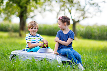 Naklejka na ściany i meble Two happy children playing with big old toy car in summer garden, outdoor