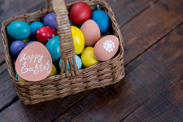 Background image of wicker basket with colorful Easter eggs in on rough wooden table with Happy Easter note