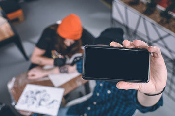 Phone in male hands in front of tattooing process in studio