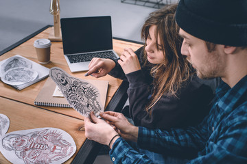 Young couple choosing tattoo design in studio