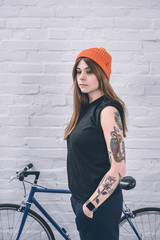 Stylish girl with tattooed arm standing next to bicycle by the wall