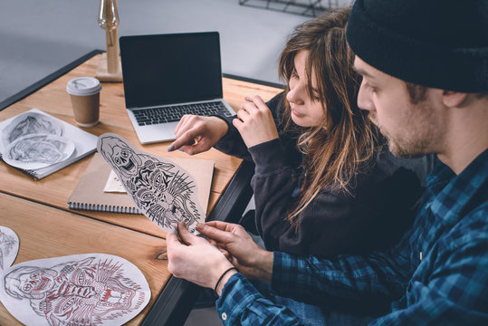 Young couple choosing tattoo design in studio