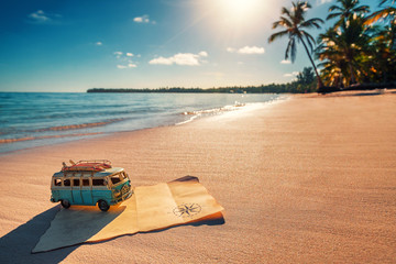 Vintage miniature van and old treasure map on the tropical beach at sunrise, travel concept