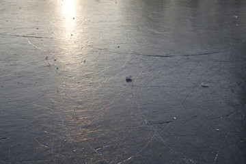 Superficie helada de lago. El sol refleja sobre el hielo. Hay trocitos de hielo sueltos.