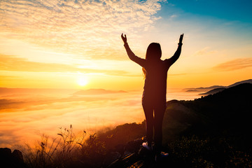 Fototapeta premium Young woman standing on top of the mountain watching the sun rise with fog
