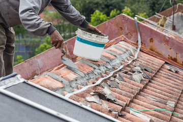 Asian worker secure roof tiles with cement on old building