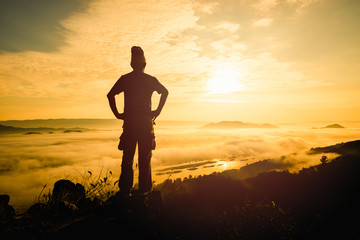 Silhouette man standing on top of the mountain watching the sun rise with fog