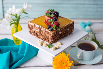 Homemade square cake decorated on top of yellow jelly and berries with mint on light background.