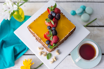 Homemade square cake decorated on top of yellow jelly and berries with mint on light background.